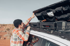 Man using the lid organizer of a low-profile 83L Rugged Case mounted on top of a vehicle